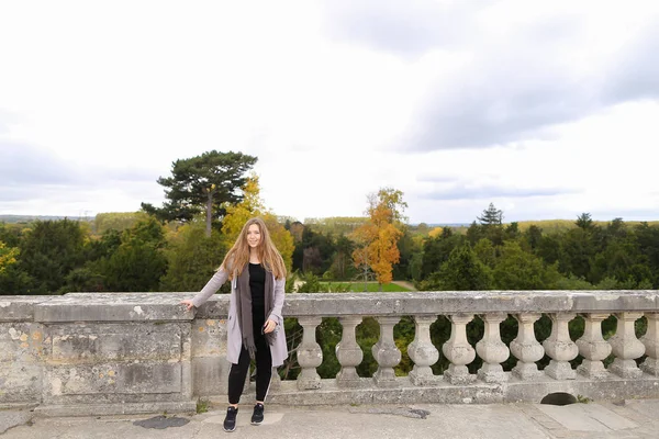 Piękna dziewczyna stojący w pobliżu betonowe balustrady, z tle drzewa. — Zdjęcie stockowe