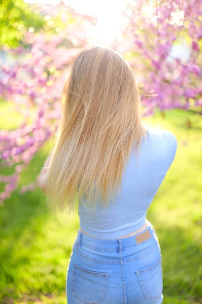 Ung flicka stående i solen strålar med grönt gräs och blossom bakgrund. — Stockfoto