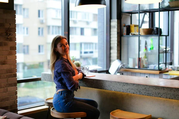 Attraktives Mädchen sitzt in Bar im Café und trägt Jeans. — Stockfoto