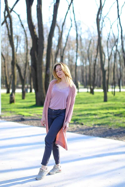 Fröhliches Mädchen ruht sich im Park aus und trägt einen langen hellrosa Pullover. — Stockfoto