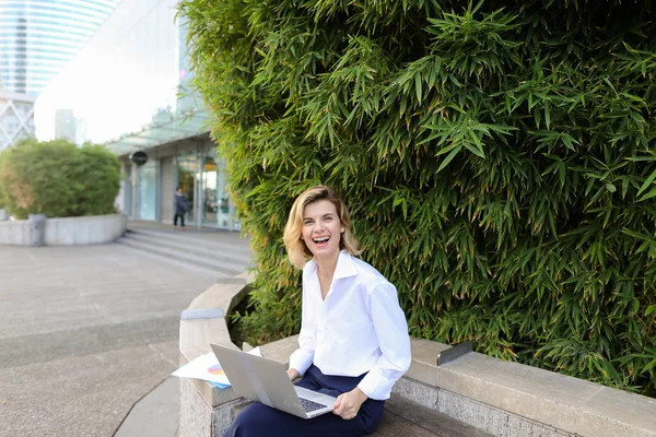Mujer de negocios sonriente trabajando con el ordenador portátil y papeles al aire libre cerca de la planta verde . — Foto de Stock