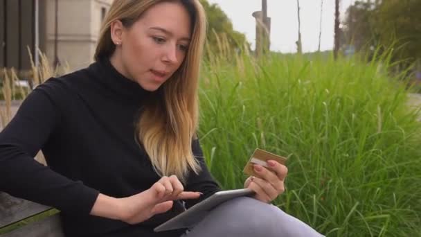 Щаслива жінка купує в Інтернеті золоту картку в парку за ноутбуком . — стокове відео