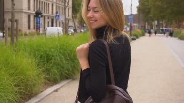 Gülümseyen, öpücük üfleme ve kameraya bakarak yola yakın, neşeli kız yürüyüş.