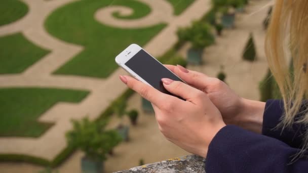 Fechar as mãos femininas digitando por smartphone com Versailles jardim fundo em câmera lenta . — Vídeo de Stock