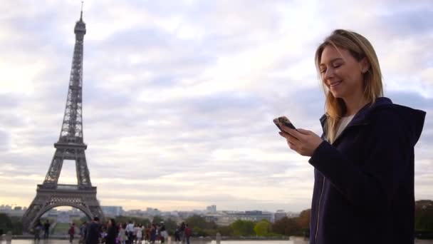 Fröhliche Frau plaudert per Smartphone mit Eiffelturm-Hintergrund. — Stockvideo