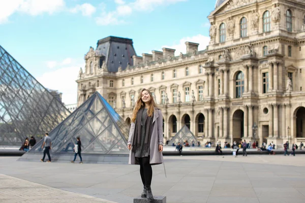 Ženská osoba na sobě šedý kabát a stojící poblíž Louvre a skleněná pyramida v Paříži. — Stock fotografie