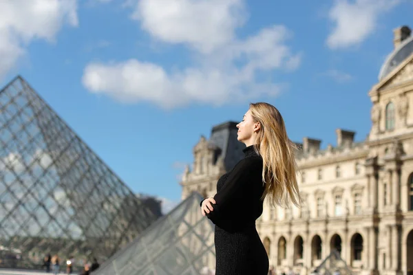 Kaukasische vrouw stond in de buurt van Louvre en glas pyramind in zwarte jurk in Parijs. — Stockfoto