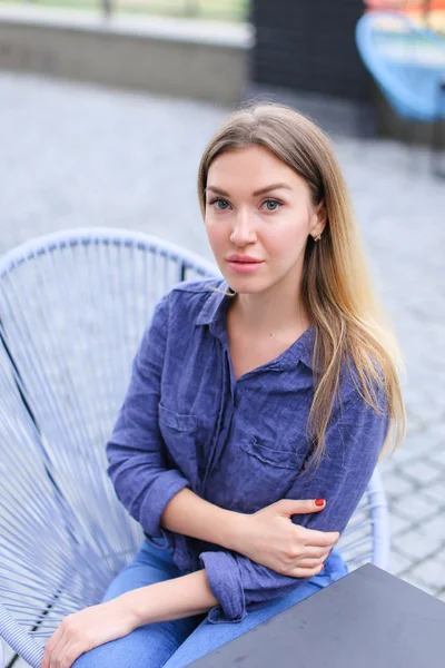 Pretty female person sitting at cafe outside and wearing blue shirt. — Stock Photo, Image