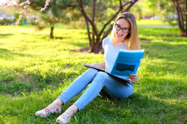 Parkta eğitim ve yeşil çimenlerin üzerinde oturan mutlu kız.