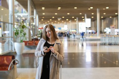 Havaalanı salonu valiz ile gidiş ve smartphone kullanarak beyaz kadın.