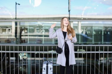 Yükseltilmiş el, valiz ve smartpone Havaalanı yakınında duran Amerikan kadın.