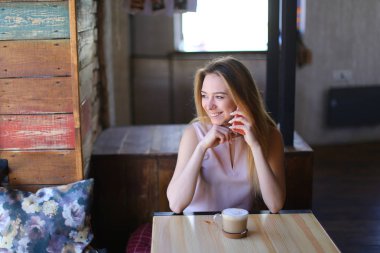 Kahve tabloyla yakınındaki rahat kafede oturan ve smartphone kullanarak Bayan.