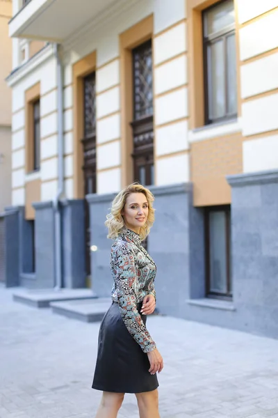 Ganska kvinnliga foto modell står nära byggnaden i bakgrunden och bär läder kjol. — Stockfoto