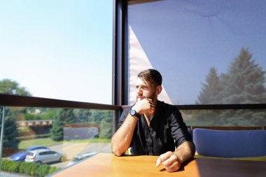 Düşünceli erkek ekolojist ofiste arka planda ağaçları ile kanepede oturan.