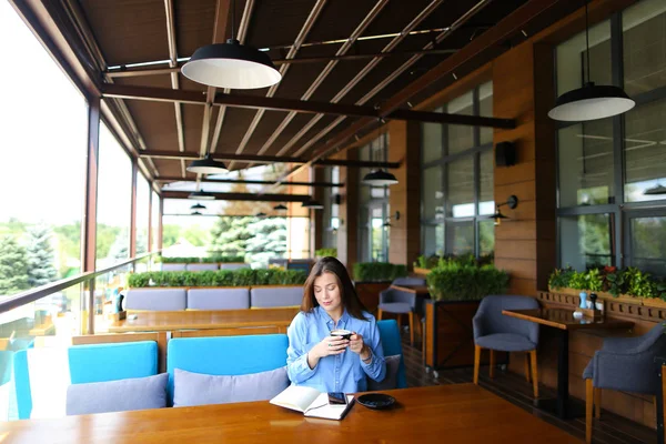Θηλυκό άτομο πίνει καφέ στο café και να κάθεται με το smartphone και σημειωματάριο. — Φωτογραφία Αρχείου