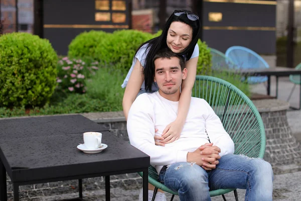 Charmante Frau umarmt Ehemann sitzt im Stuhl in Straßencafé draußen. — Stockfoto