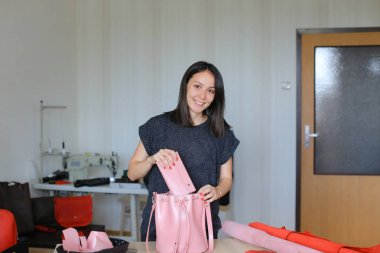 Kız pembe el yapımı deri kadın çanta ve cüzdan ile bir atölye ayakta.