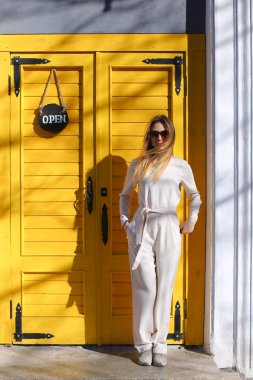 Sarışın Amerikan Kız Beyaz takım ayakta kafe kapı yakınındaki güneş ışınları giyiyor.