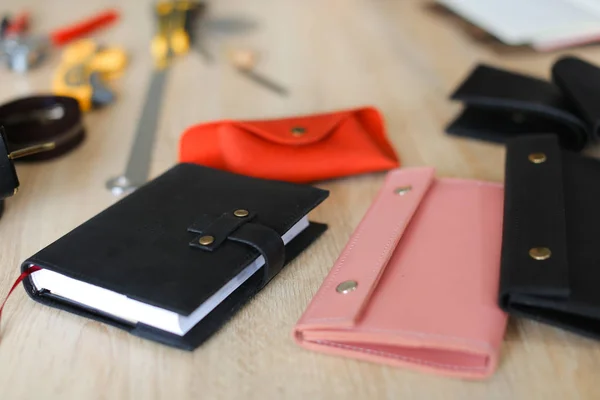 Black and pink handmade leather fashionable wallets and notebook lying on table.
