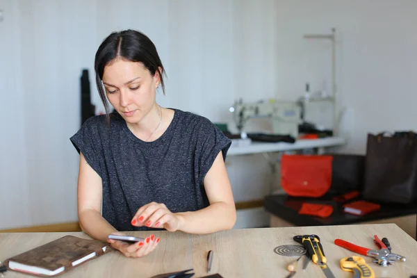 Artigiana americana seduta in atelier e con smartphone, pelletteria artigianale . — Foto Stock