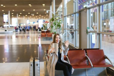 Tablet Havaalanı salonunda görüntülü arama yapma ve valiz oturan kadın.