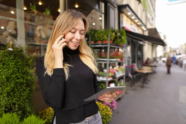 Mujer de negocios caucásica de pie con la tableta y hablando por teléfono inteligente cerca de la tienda de flores . — Foto de Stock