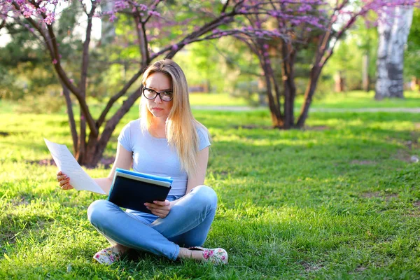 Travailler dur étudiant féminin assis sur l'herbe verte avec dossier noir annonce lecture . — Photo