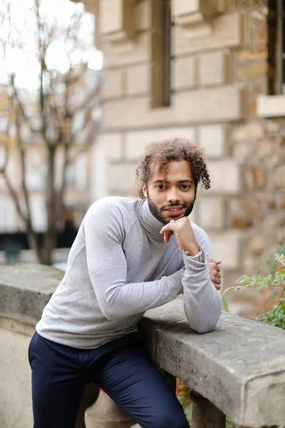 Schwarzer gutaussehender Junge in grauem Rollkragenpullover, der in der Nähe von Betongeländern in der Nähe von Backsteinmauern steht. — Stockfoto