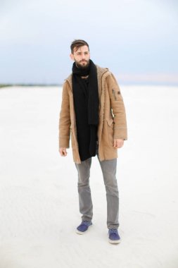 Paltonu ve kaşkolünü beyaz kar arka planda duran giyen beyaz adam.
