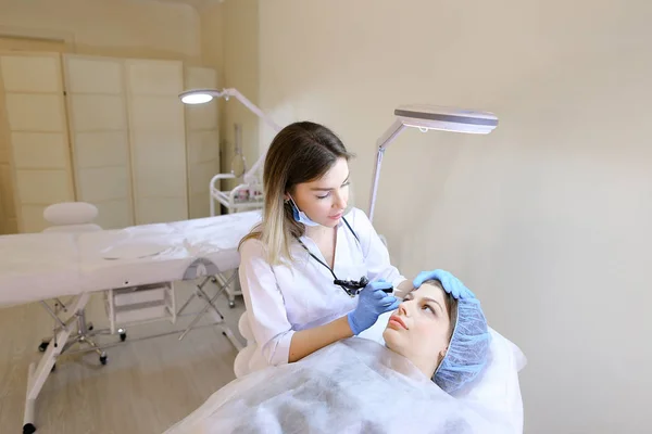 Lady lying at cosmetology cabinet and getting tattooing eyebrows.