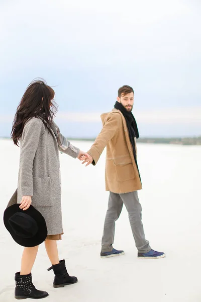 Чоловік і жінка йдуть на сніг і тримаються за руки, одягнені в пальто і шарфи . — стокове фото