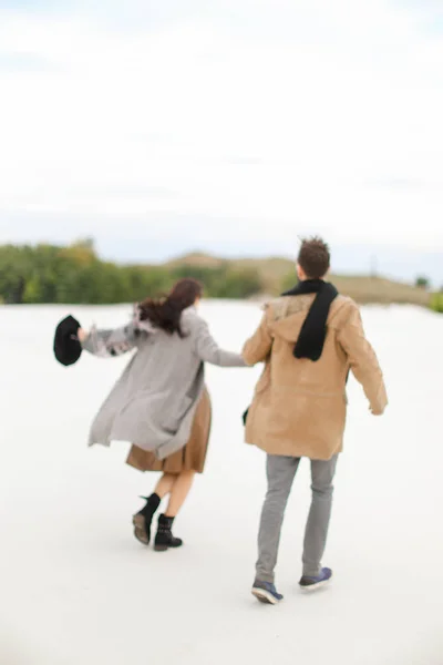 冬の白背景で幸せなカップルが歩いて、手を繋いでいるとコートを着て. — ストック写真