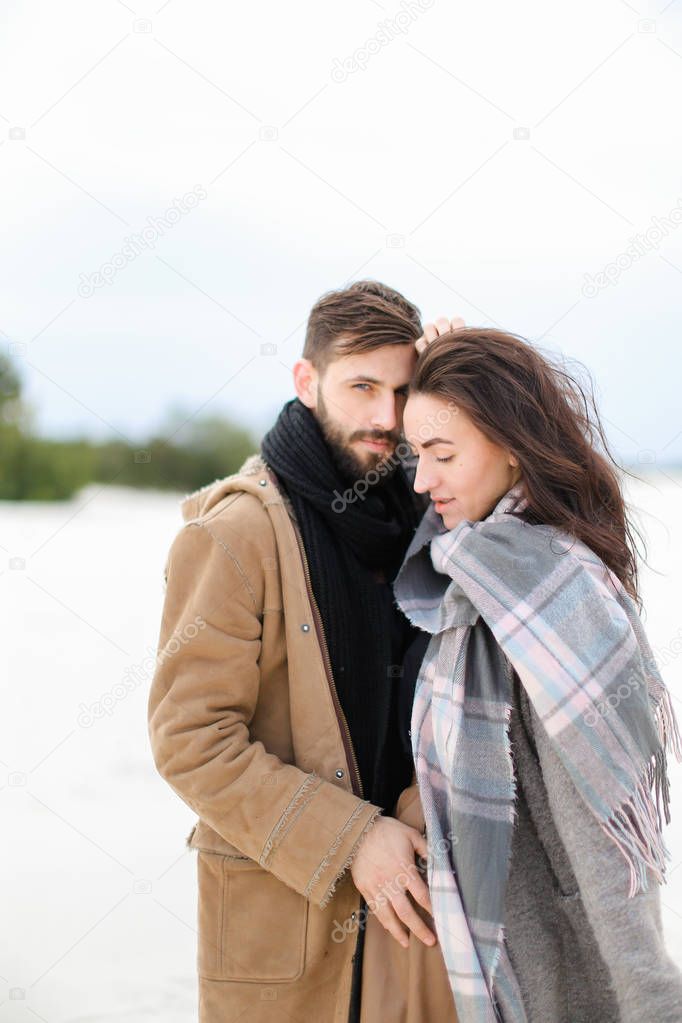 Young nice woman wearing grey scarf standing with man in coat, winter white background.