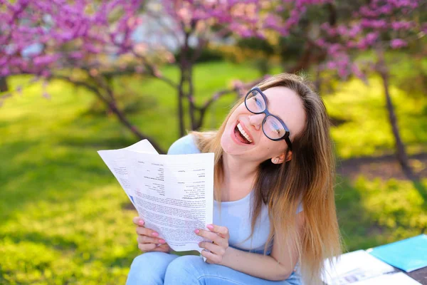 Laughing female student reading papers and studying in spring park.