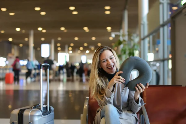 Girl sitting with neck pillow and luggage in airport waiting room. — Stock Photo, Image