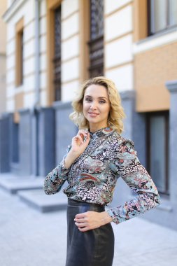 Çevre binanın önünde duran deri etek giyen genç kadın.