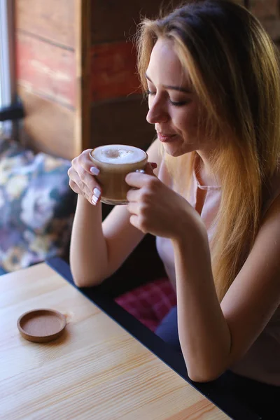 Kobieta siedzi w pobliżu okna filiżankę kawy i pozowanie do zdjęć. — Zdjęcie stockowe