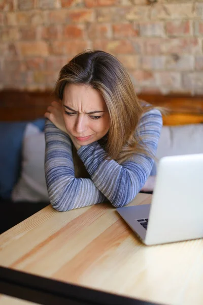 Young woman sitting in cozy coffee house near wooden table with glass cup of cappuccino and using laptop.