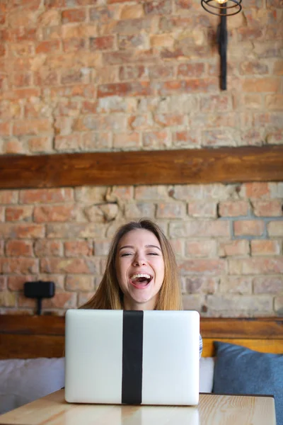 Riéndose chica disfrutando con el ordenador portátil en la cafetería y haciendo caras . — Foto de Stock