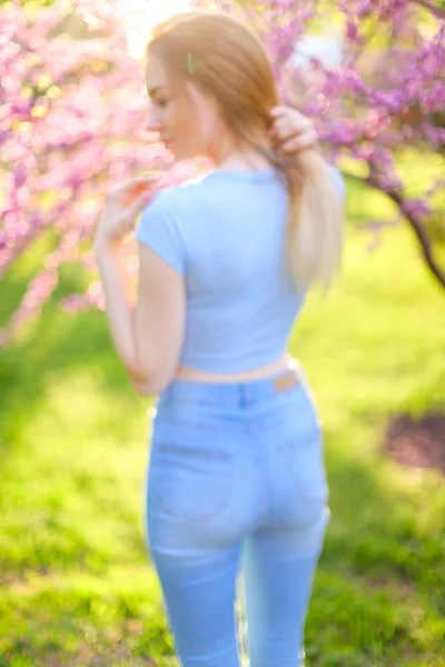 Flicka klädd i jeans stående i solen strålar med blommande grenar bakgrund. — Stockfoto