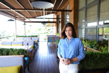 Smartphone ile ayakta ve kot gömlek ve beyaz pantolon giyen kafe Müdürü.