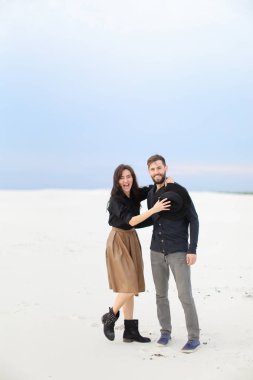 Etek ve siyah gömlek giyen genç çift Kış kar tek sesli arka planda, sarılma gülümseyen.