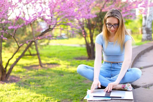 Étudiante assise avec ordinateur portable dans un parc en fleurs . — Photo