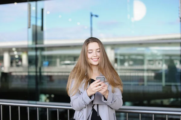 Mujer caucásica mensajes de texto por teléfono inteligente cerca de valise y aeropuerto . — Foto de Stock