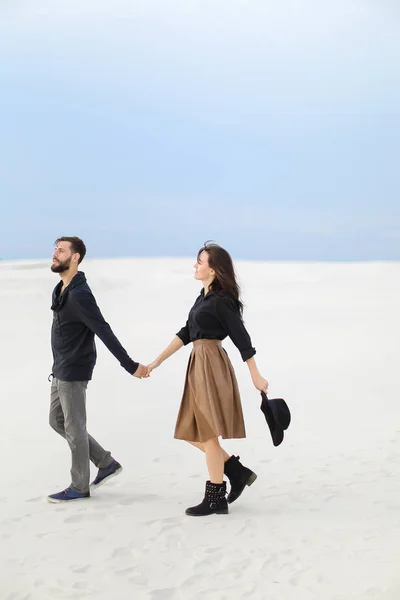 Caucasian couple walking on snow, holding hands and wearing skirt and jeans.