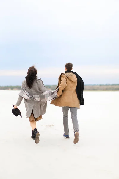 冬の白背景で幸せなアメリカ人カップルが歩いて、手を繋いでいるとコートを着て. — ストック写真