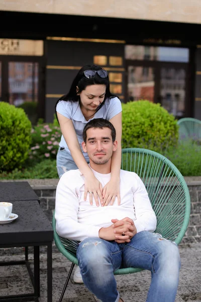 Brünette Frau umarmt Mann sitzt im Stuhl im Straßencafé draußen. — Stockfoto