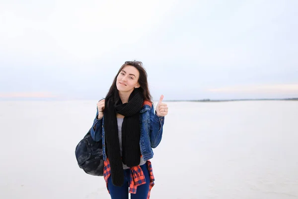 Mulher caucasiana vestindo jeans e bolsa, mostrando os polegares para cima e de pé em fundo de inverno branco . — Fotografia de Stock