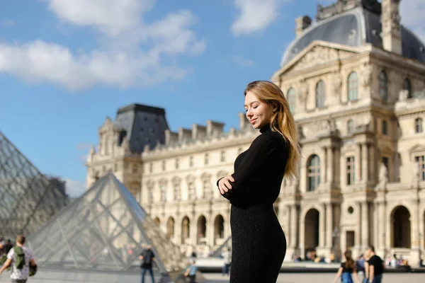 Kaukasiska flicka som står nära Louvren och glas pyramind i svart klänning i Paris. — Stockfoto