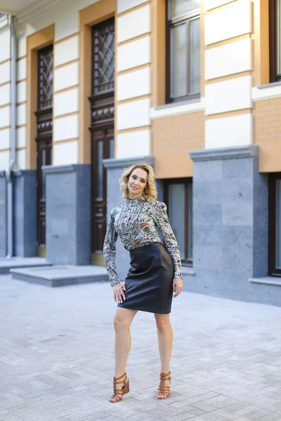 Female photo model standing near building in background and wearing leather skirt. — Stock Photo, Image